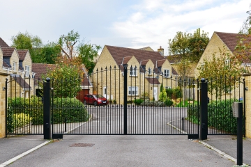 Traditional black wrought iron home electric gates with decorative finials and a curved design, enhancing the kerb appeal and security of a residential driveway.