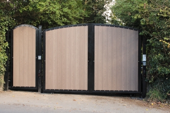 Bespoke home electric gates with wood-effect panels, black metal frames and matching pedestrian gate, creating a stylish, secure driveway entrance.